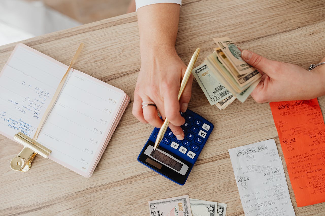 Hands managing finances with calculator, cash, and receipts on a wooden table. Ideal for budgeting concepts.